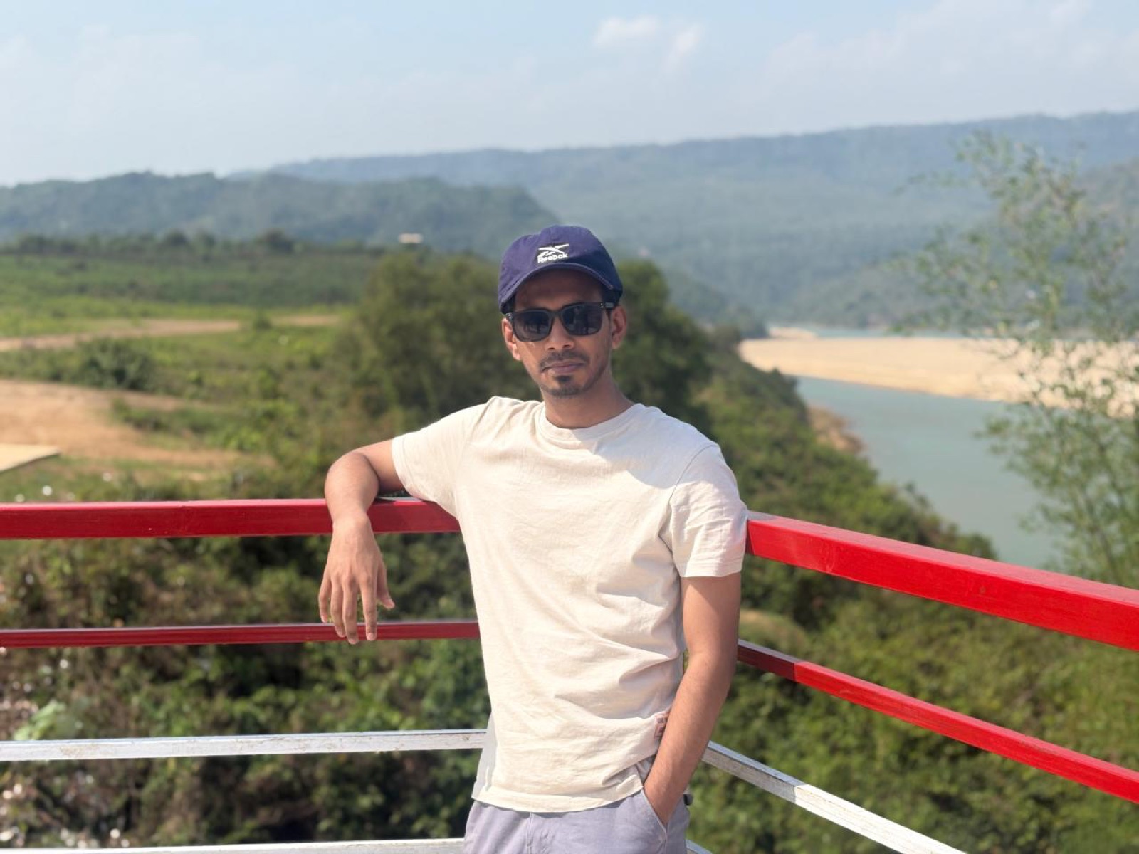 Leaning on a red railing overlooking a river and hills