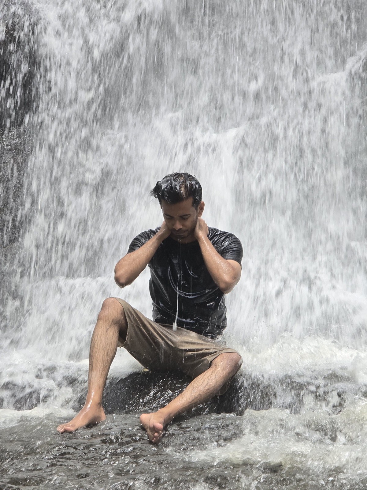 Sitting under a waterfall, hands on neck, eyes closed